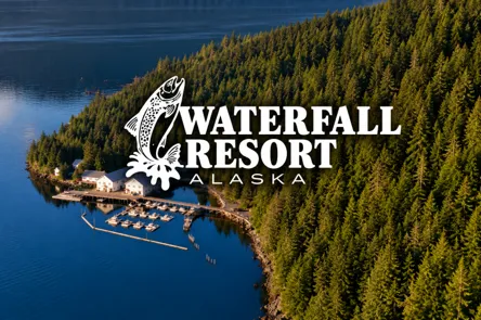 LLSRace - Aerial view of Waterfall Resort Alaska, featuring docked boats, buildings by the water, and dense forest on a sloping shoreline. - Love Like Sean Race
